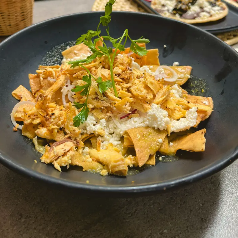 Chilaquiles con queso fresco y cilantro en plato de barro negro